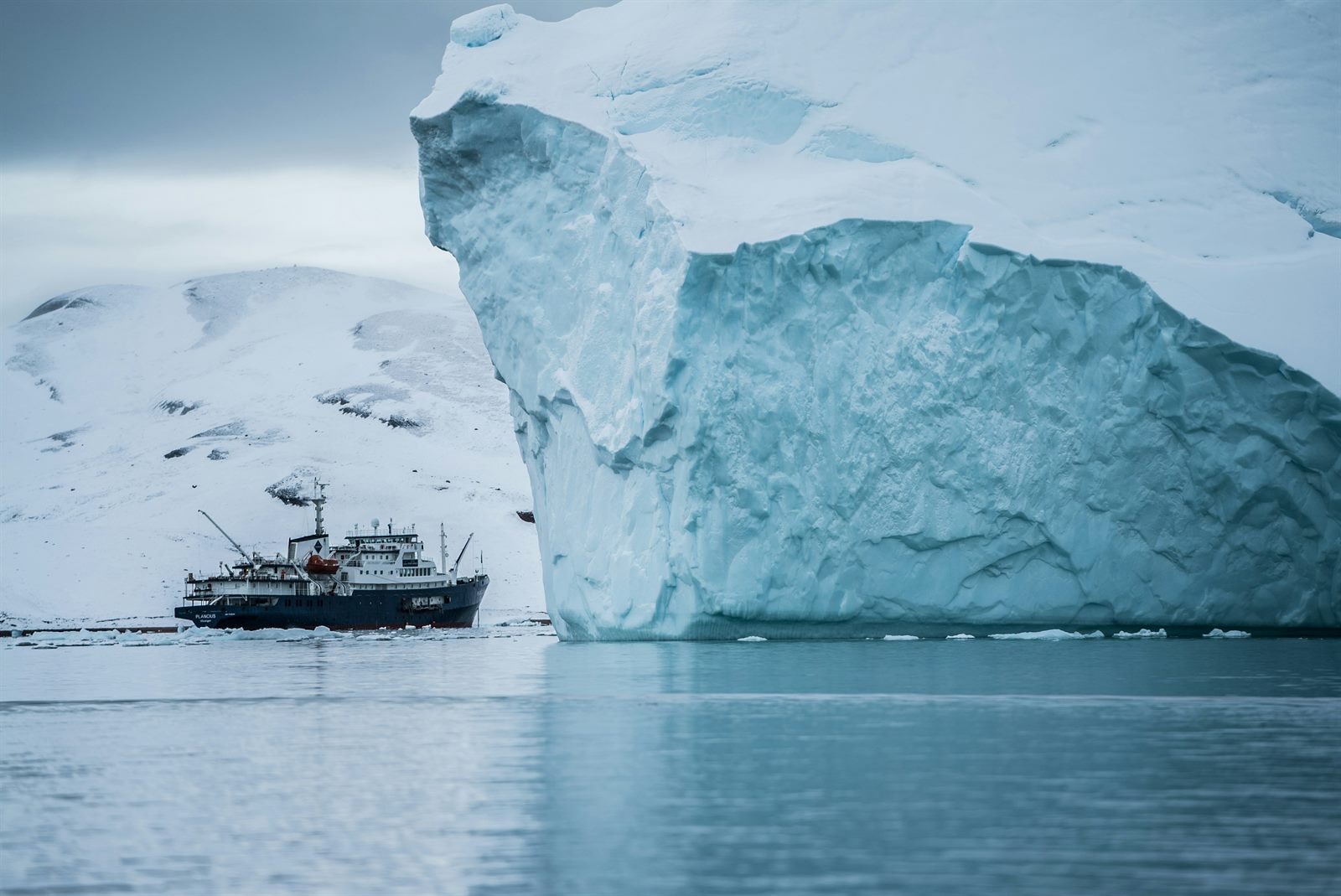 A red-hulled icebreaker cutting through cracked sea ice under a low Arctic sun, open dark water in its wake