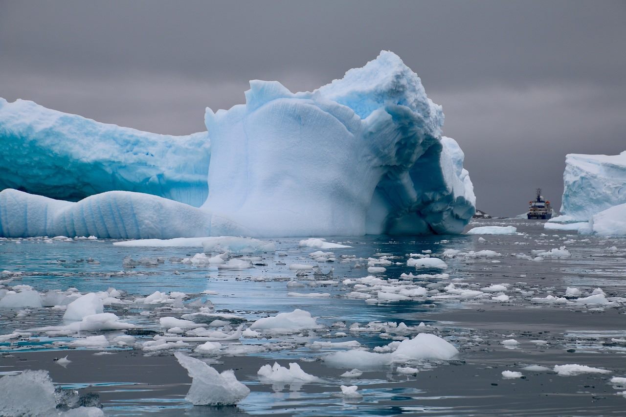 A cargo ship escorted by an icebreaker along an open Arctic shipping lane with coastal radar installations on the horizon