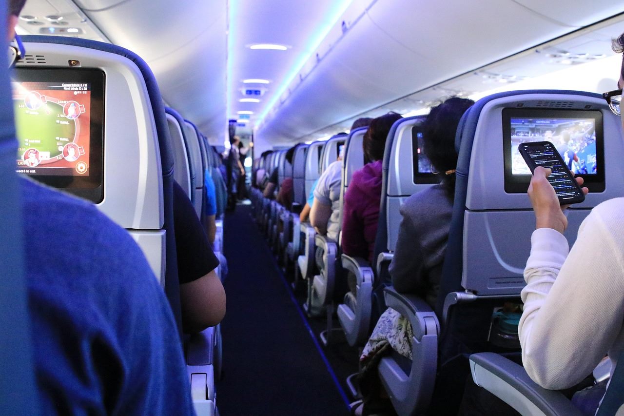 Passengers watching a departures board where budget airline fares tick upward next to a new carbon surcharge line