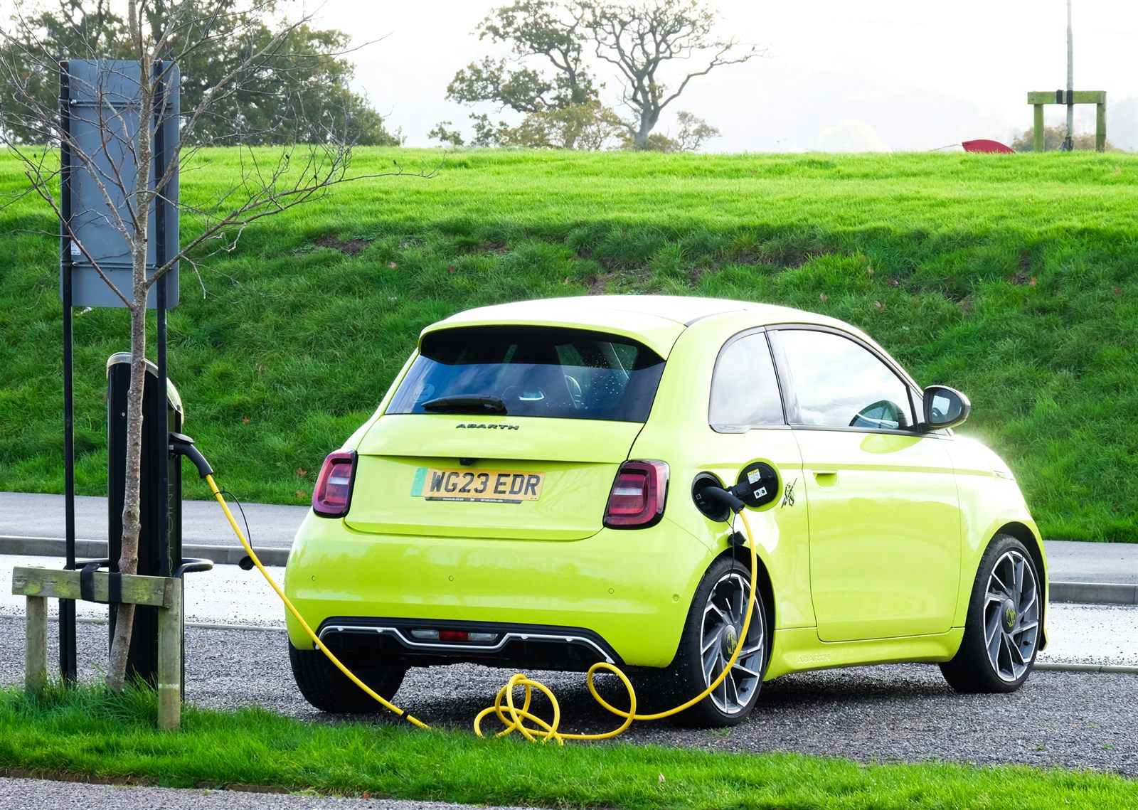 A person reviewing vehicle cost comparison figures on a tablet, with an electric car visible in the background