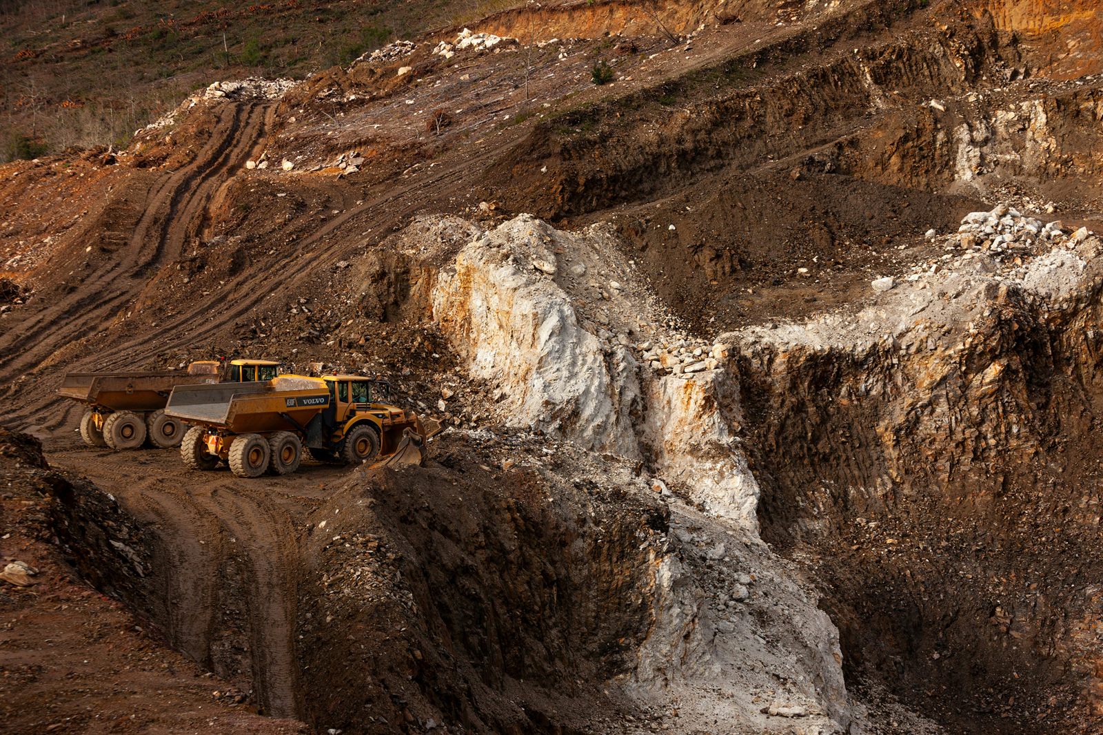 An open-pit mine terraced into red-brown rock, with haul trucks working the lower benches