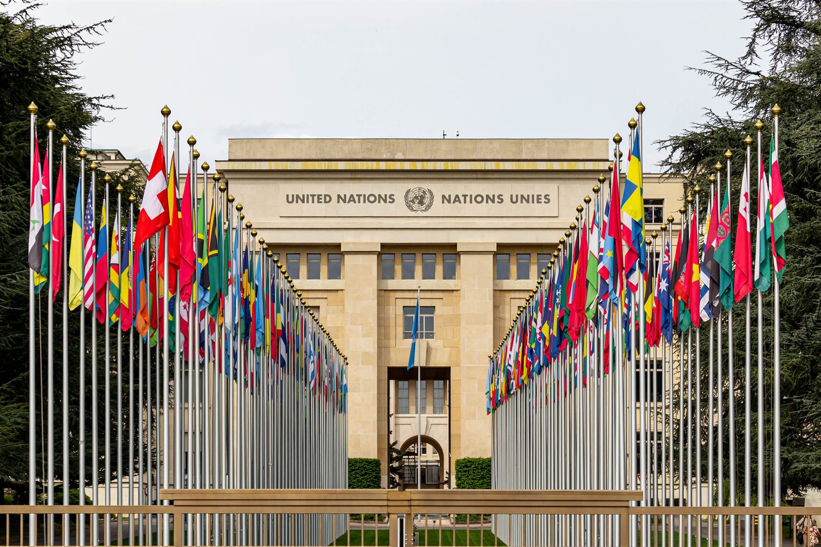 A row of national flags outside a large international headquarters building, some flags at half-mast