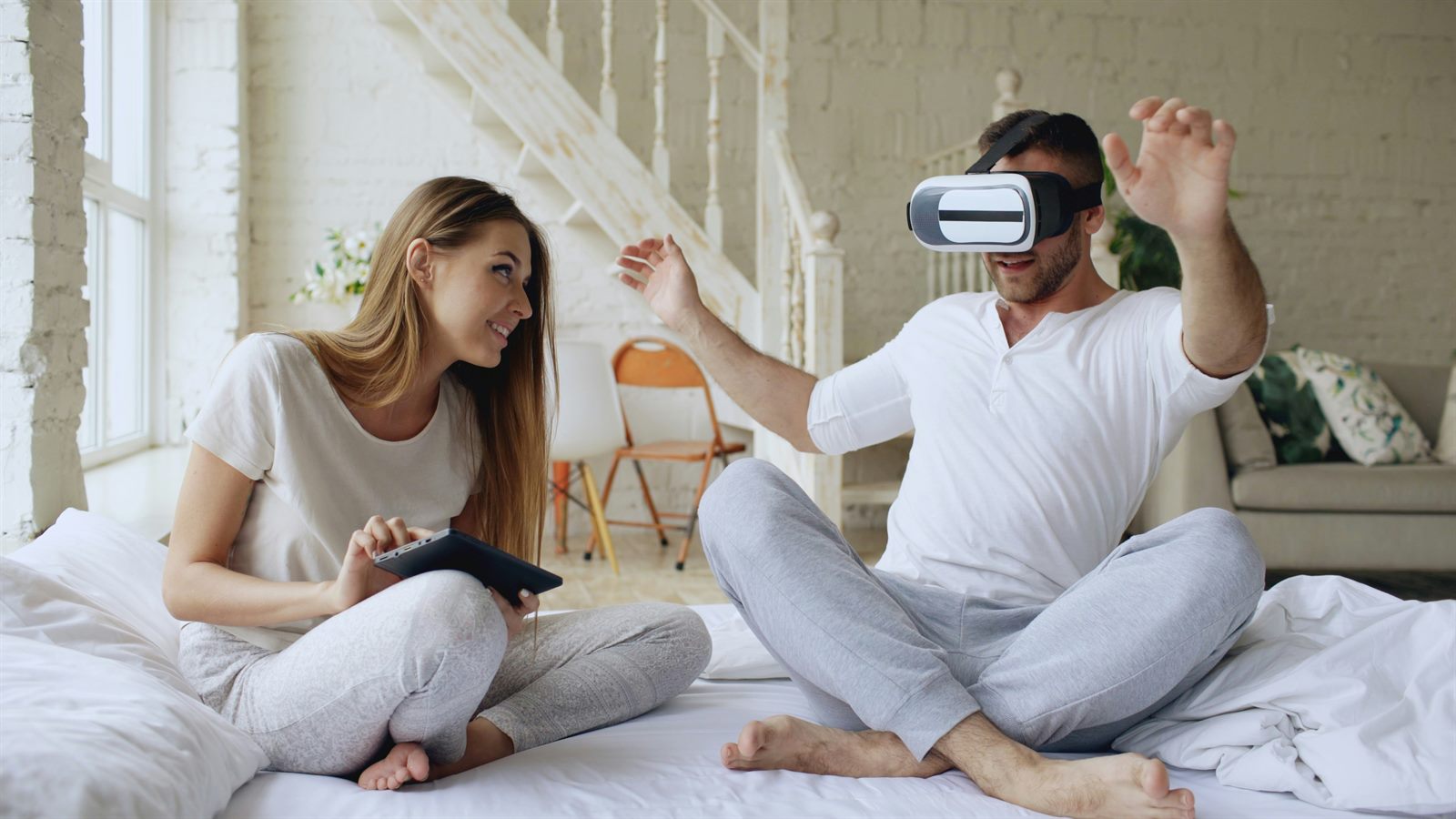 Two people sharing a VR headset in a bright living room, laughing together