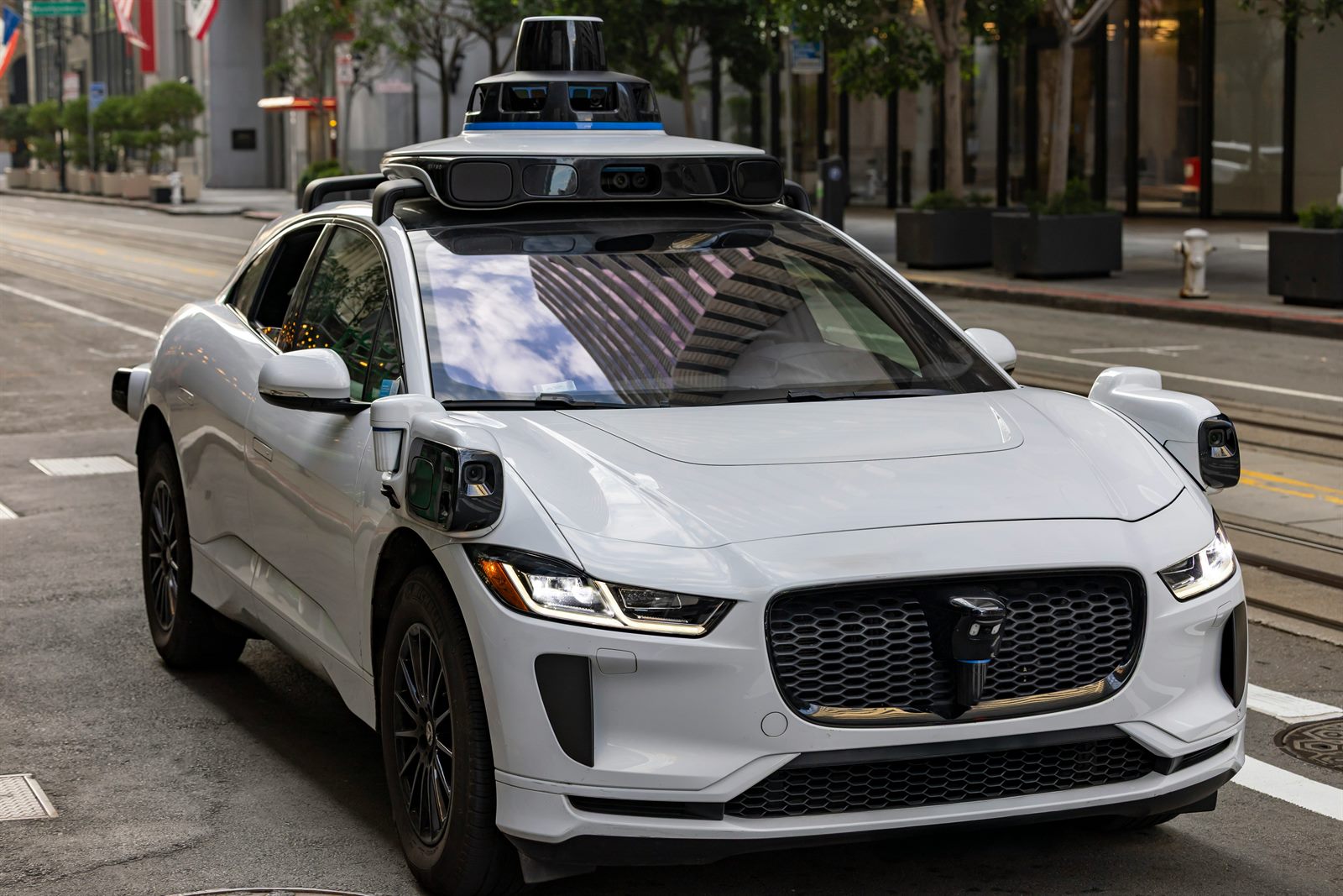A Waymo autonomous vehicle moving through a city street at dusk, no driver visible
