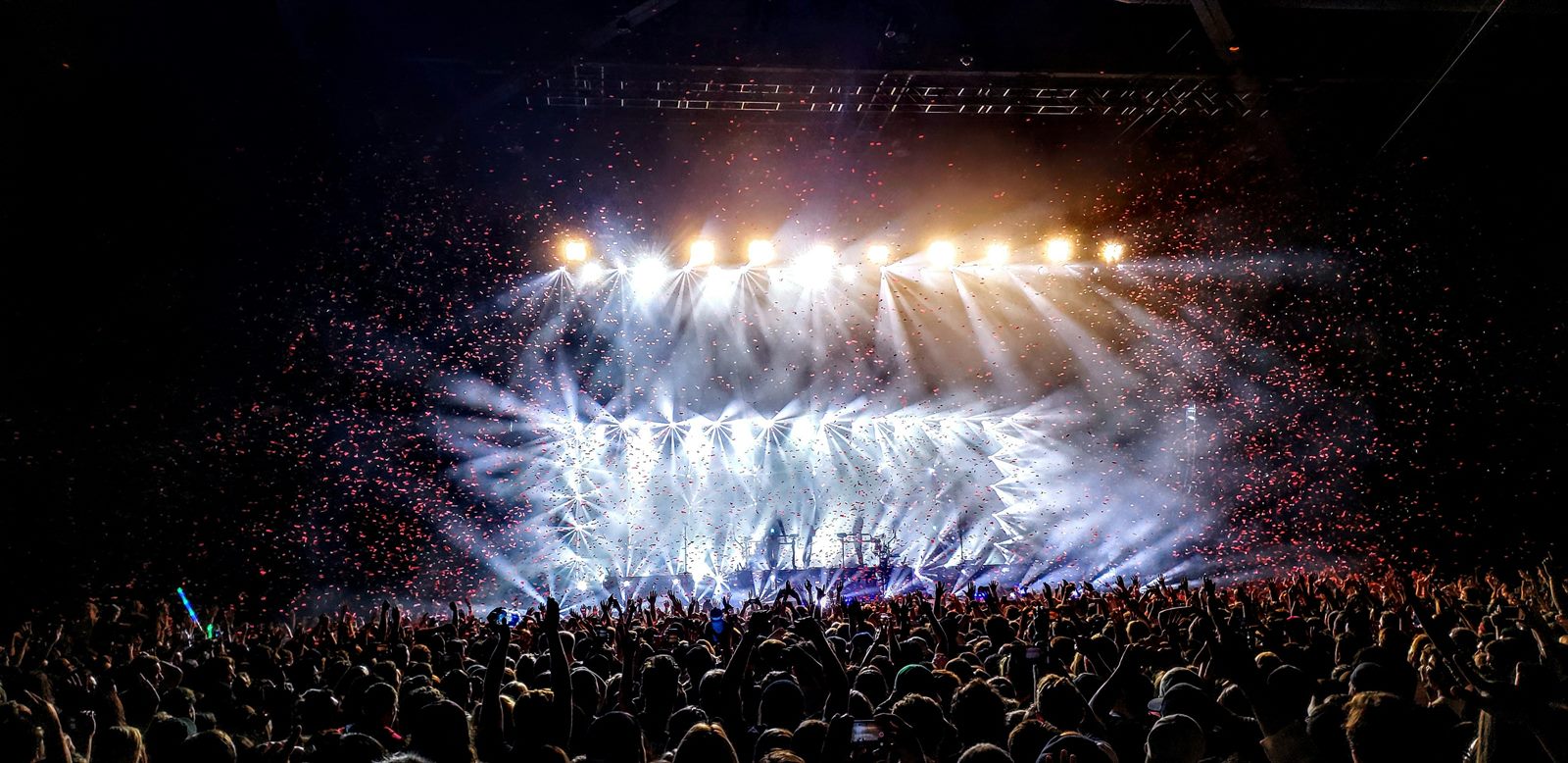 Packed stadium concert at night with phone lights glowing and a giant illuminated stage