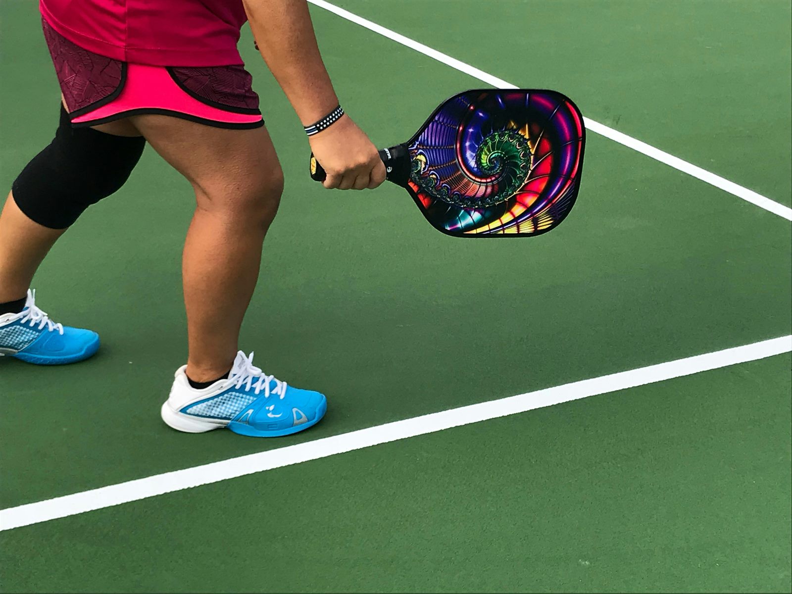 A suburban racket club aerial view showing several pickleball courts painted over a former tennis court, with players on each one