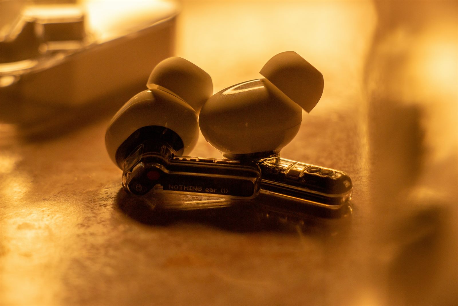 A sleek modern earbud resting in an open charging case beside a smartphone showing a hearing app