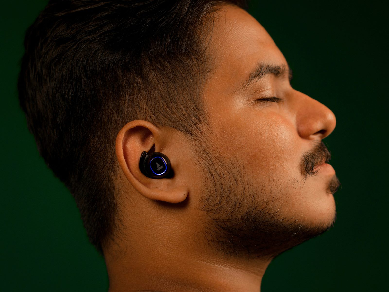 An older man smiling in conversation at a busy dinner table while wearing a discreet earbud