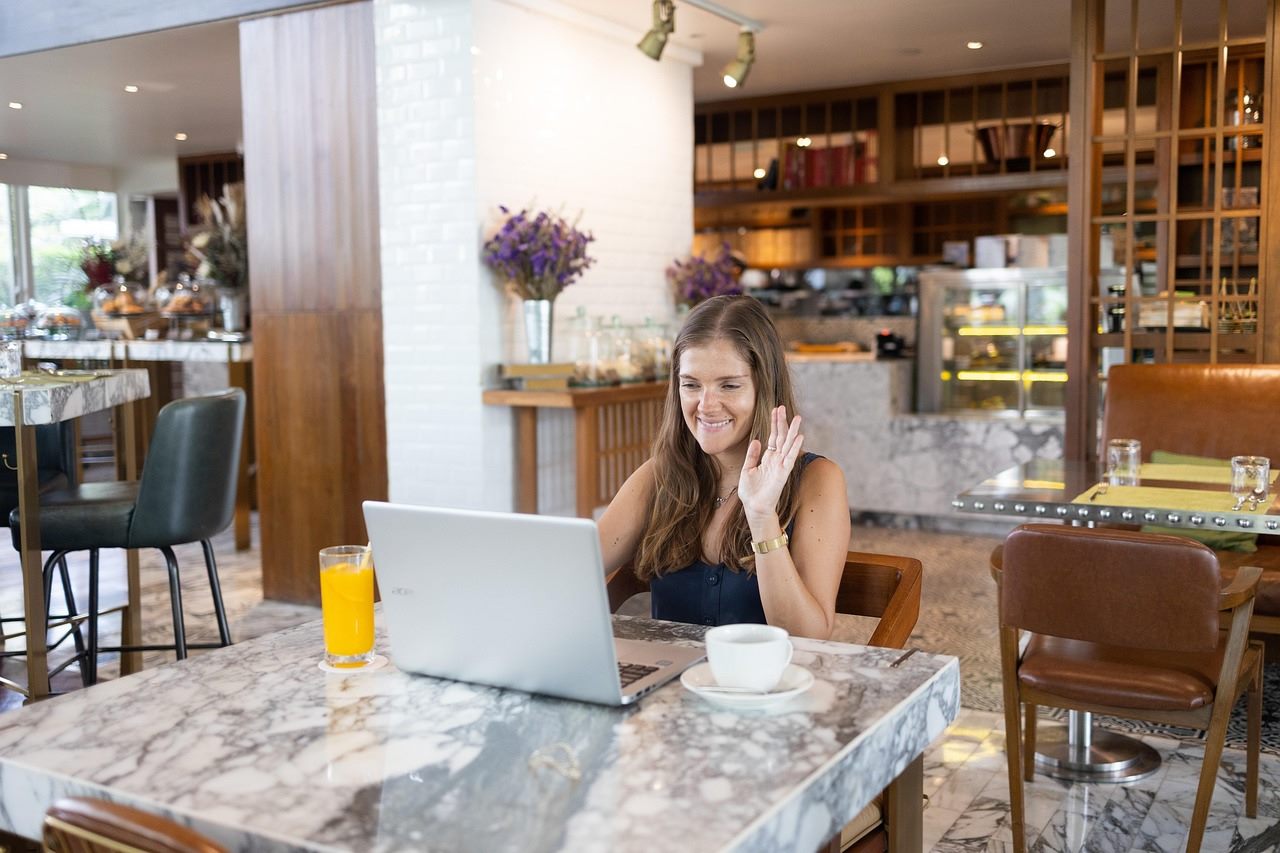A remote worker with a laptop at a sunlit co-working café overlooking a coastal town in another country